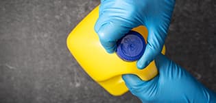 Hand in protective glove opening a bleach bottle illustrates PlusChem's expertise in Solvents