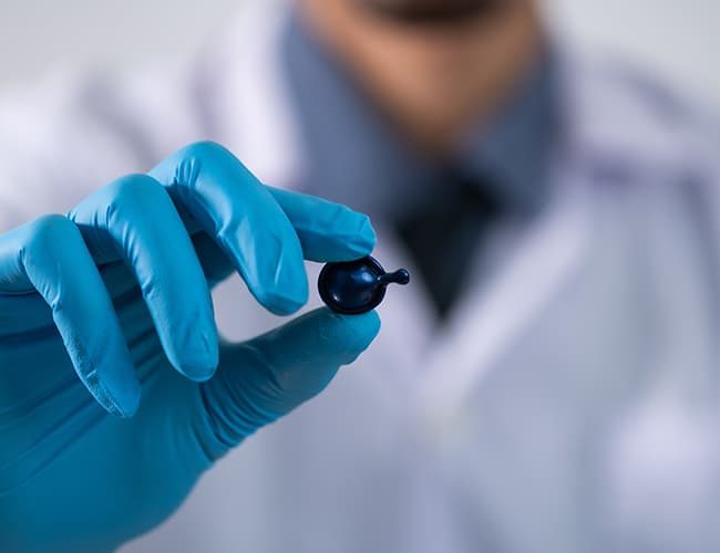 Chemist in blue protective glove holding a serum capsule illustrates PlusChem's expertise in Additives