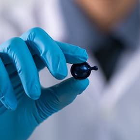 Chemist in blue protective glove holding a serum capsule illustrates PlusChem's expertise in Additives