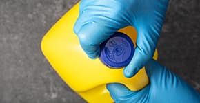Hand in protective glove opening a bleach bottle illustrates PlusChem's expertise in Solvents